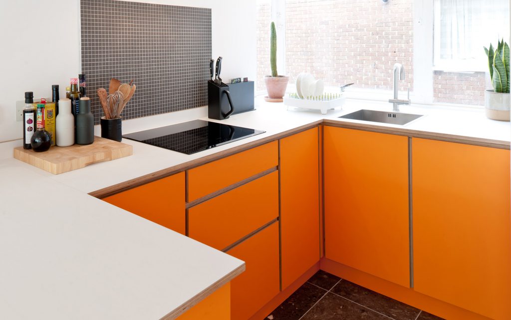 A small orange plywood kitchen with white worksurface - a bespoke kitchen created from scratch by the Koivu team.