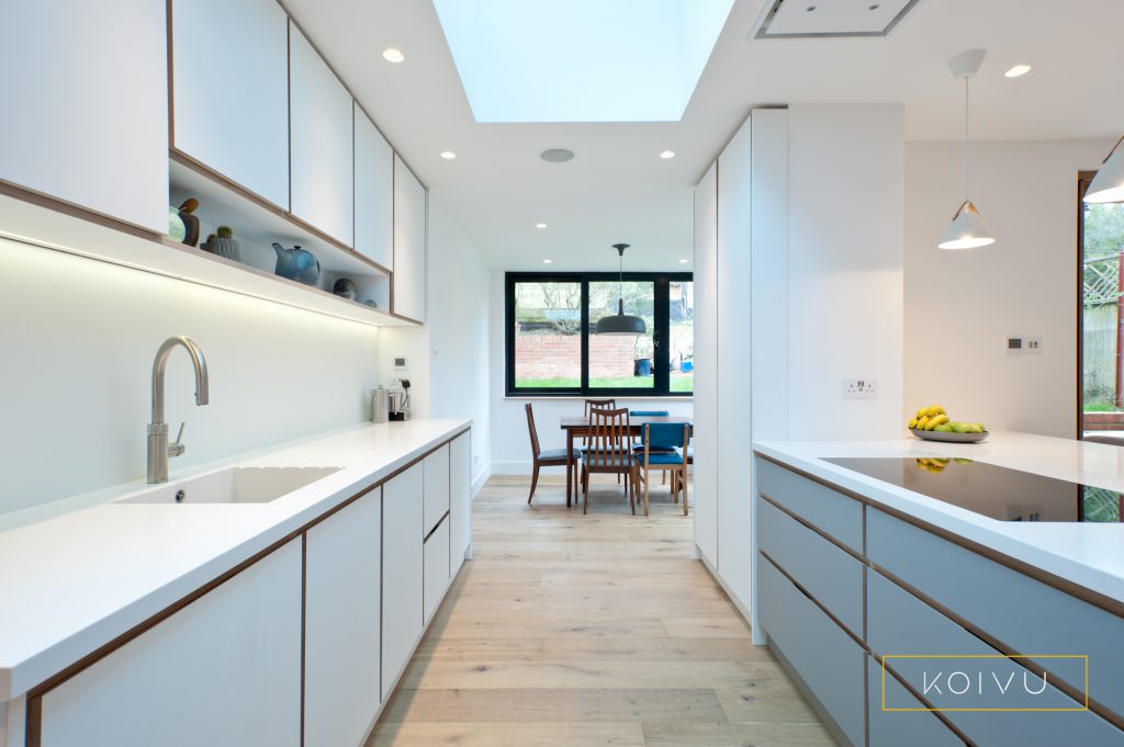 A white and grey plywood kitchen designed for a couple in Crystal Palace. Grey drawers in the island contrast with the bank of white wall units.