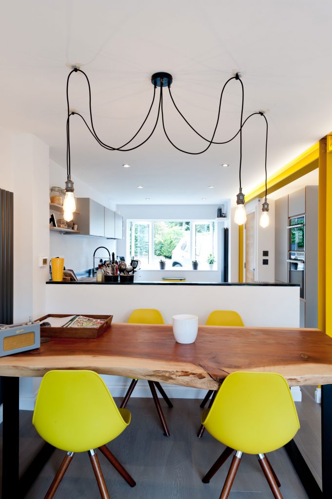 Koivu grey kitchen in background with beautiful solid wood table and yellow chairs in foreground. 