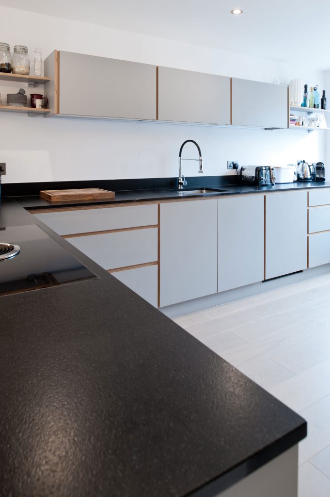 L-shaped pale grey kitchen with black worktop. Showing sink in long run and Bora hob in peninsula. By Koivu.