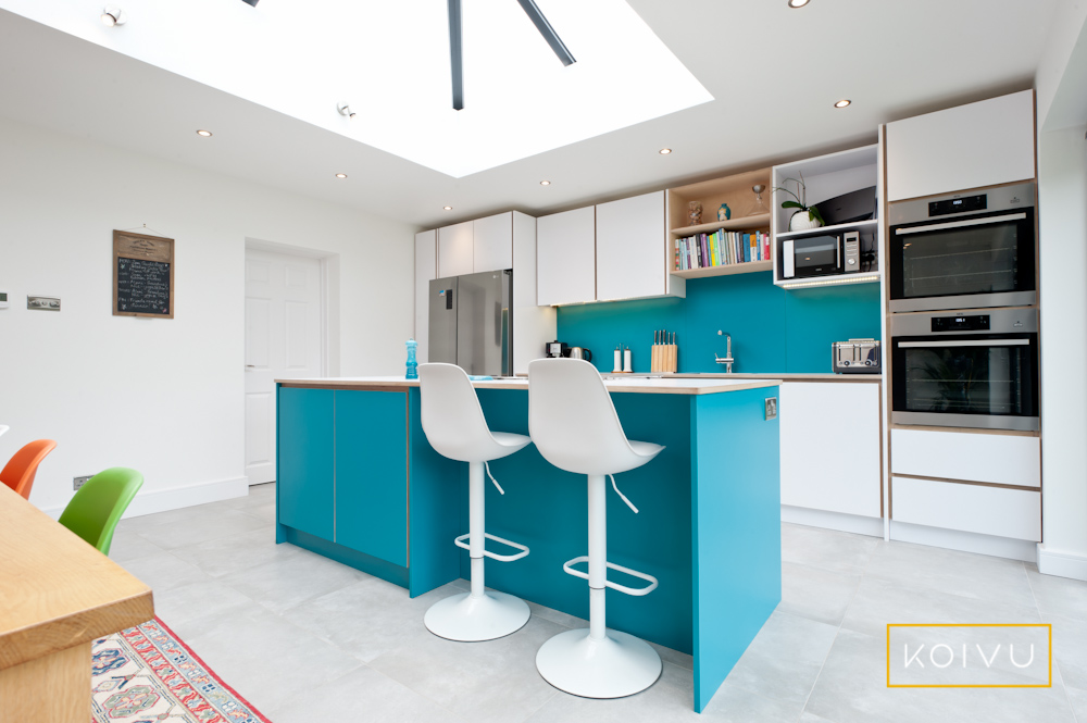 A small kitchen extension housing a white and turquoise kitchen designed by Koivu. 