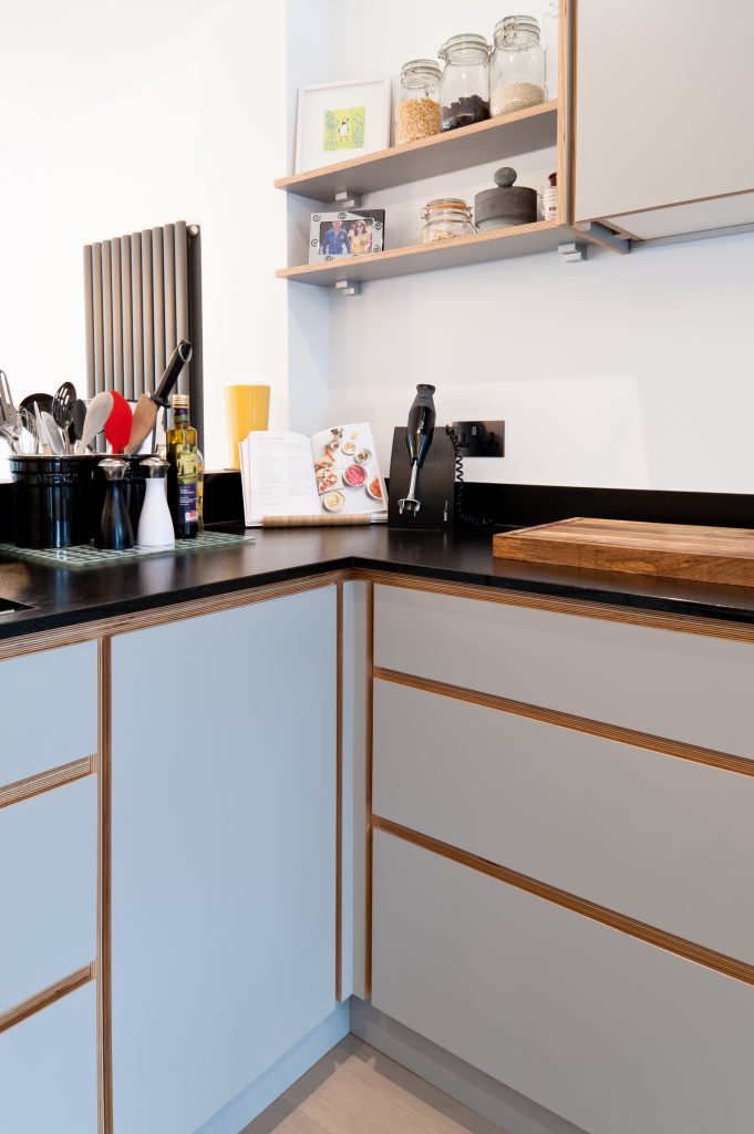 A white plywood kitchen with wood detailing and thin black work surface and open shelves