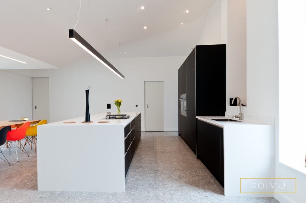 Side view of large kitchen extension. Tall, black kitchen cabinets, large island and white worktops. Bespoke birch plywood design by Koivu.