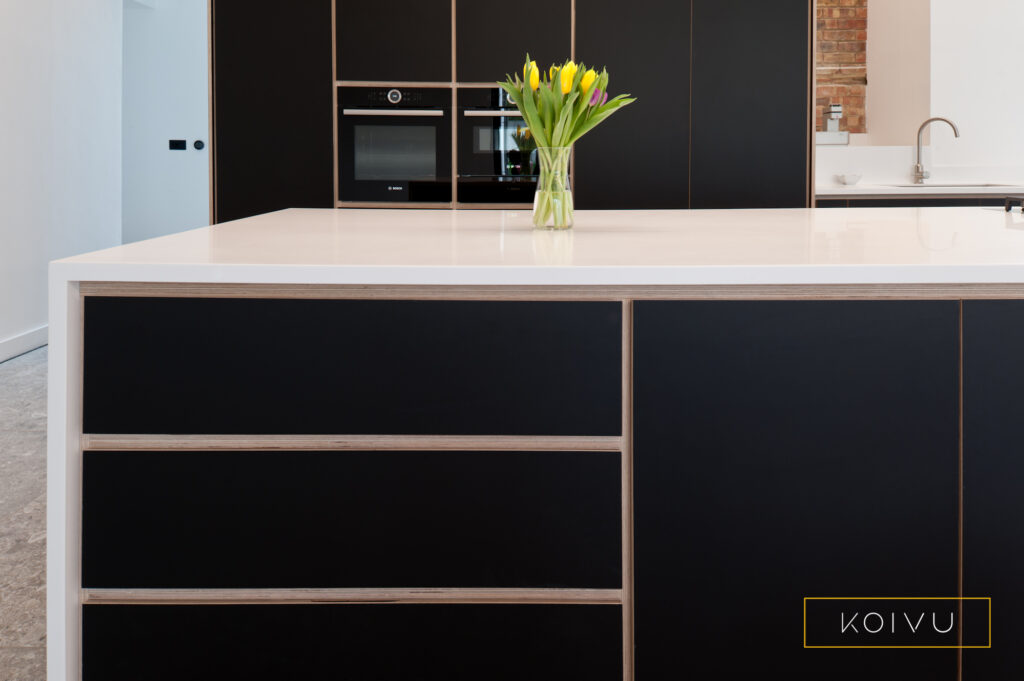 Minimalist kitchen design showing off tall black oven housings behind with large island with storage in the foreground. 