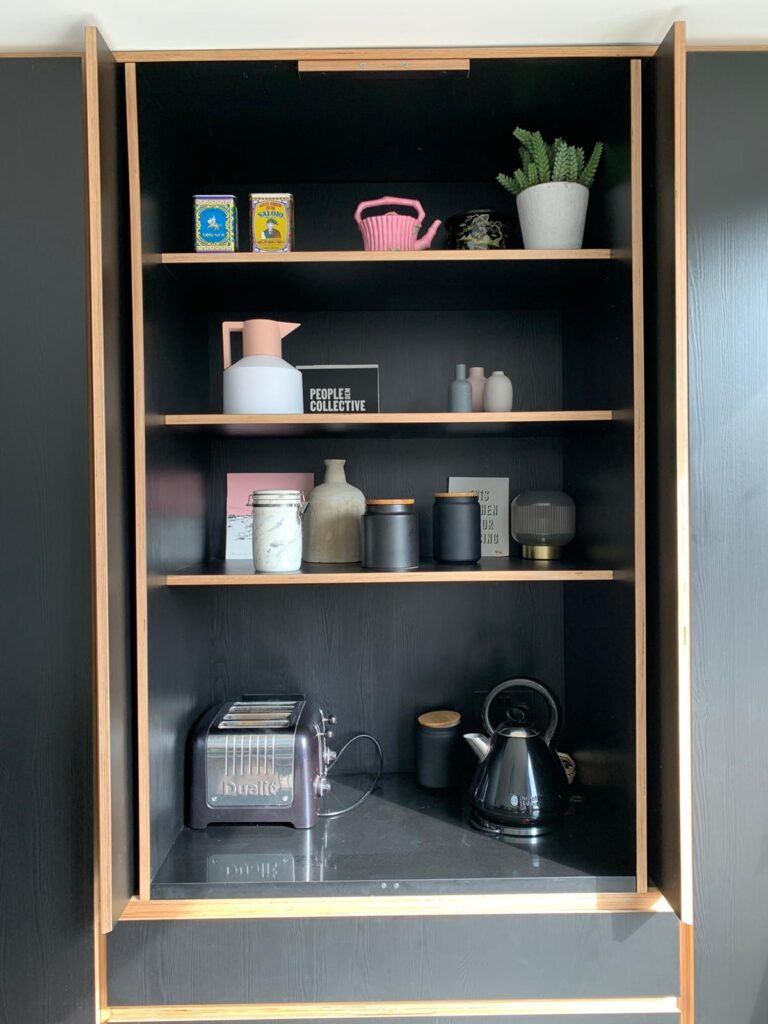 A picture of a bespoke designed black plywood Butler's Cupboard with pocket doors that have been opened up and folded back to create space.