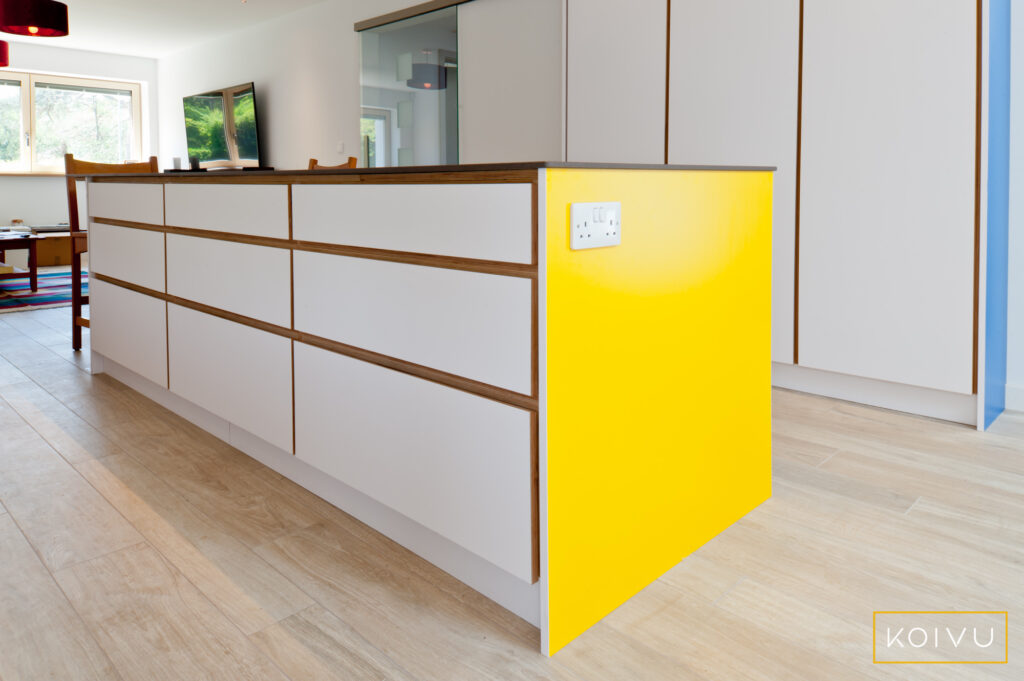 Large kitchen. Drawer units in white island with yellow end panel and no handles.