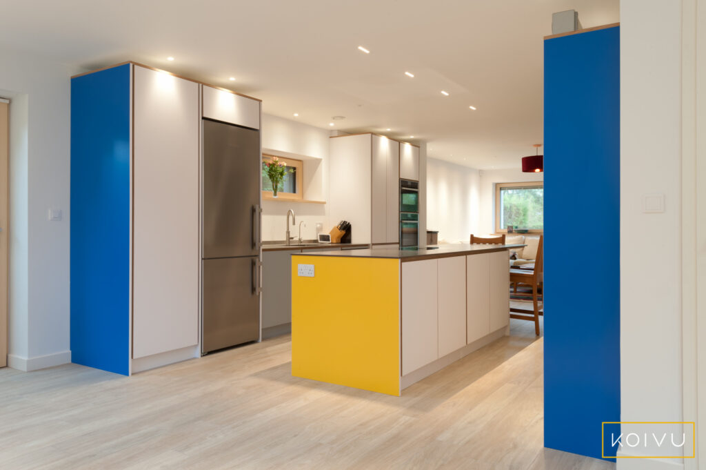 A white galley kitchen with splashes of yellow and blue. Designed in birch plywood with thin, modern worktops, this kitchen was designed by Koivu. 