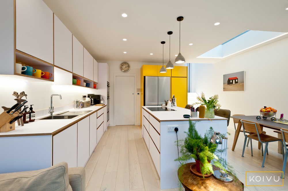 Striking white and yellow kitchen built from sustainable birch plywood. Includes island with hob, pendant lighting, under unit open shelves and tall units housing American style fridge / freezer.