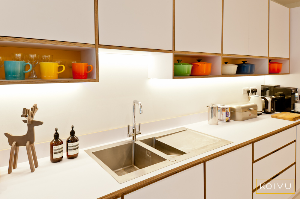 Run of white plywood units showing edge detailing. Under unit shelves and brushed stainless steel sink. BY Koivu.
