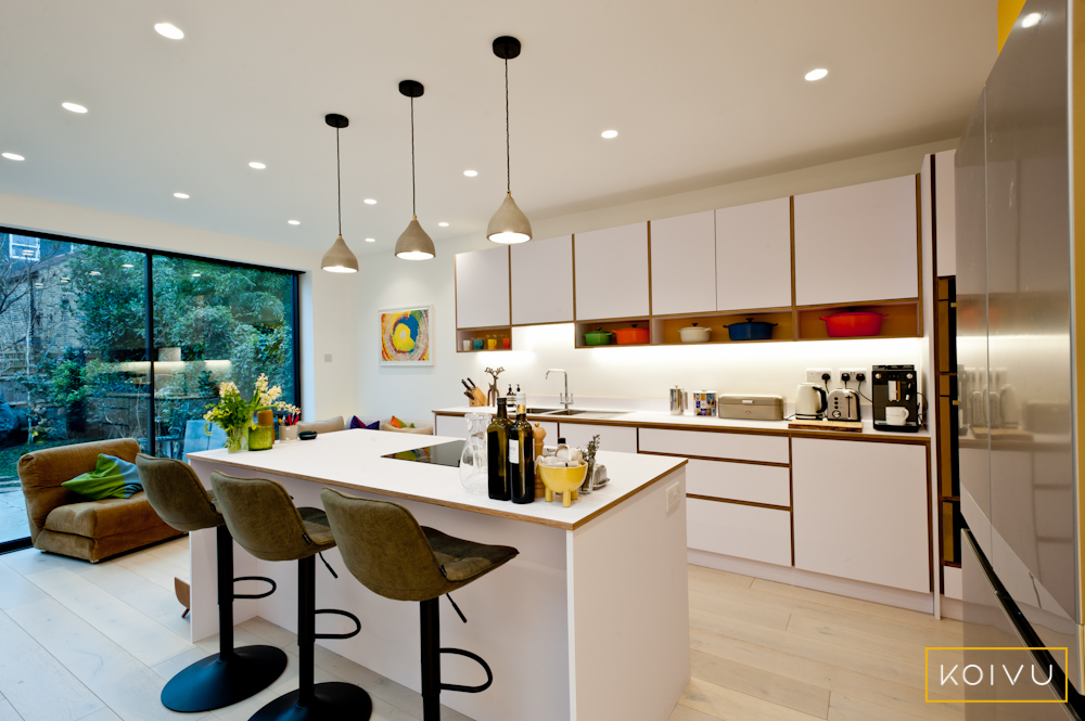 A white kitchen with open shelves and colourful accents. There is an island with sating in the foreground. Picturing what you always wish you'd had in your kitchen can help you to work out what's important to you. 