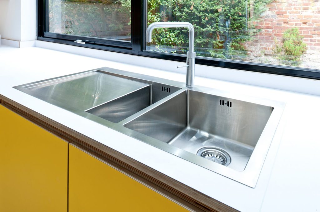 Tap, or water faucet, over a stainless steel sink in a yellow Koivu kitchen. Water conservation features in an eco-friendly kitchen