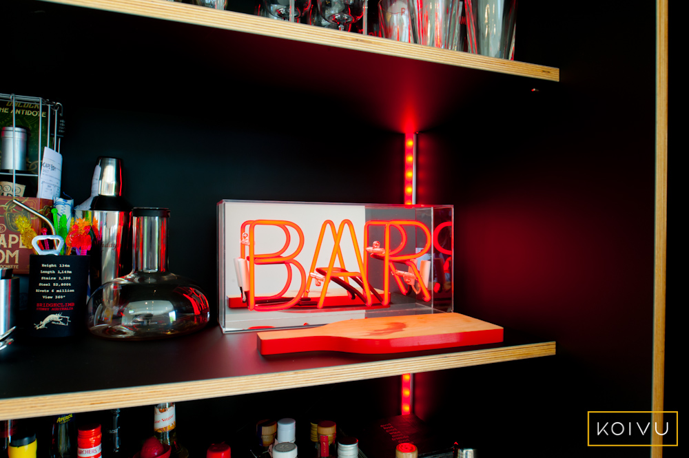 One of the kitchen design trends for 2024 is bespoke drinks areas / storage. This photo shows a bar area / butler's cupboard that was designed and made bespoke by Koivu. It features a fabulous red neon bar sign sitting on the black plywood shelving inside the cabinet.